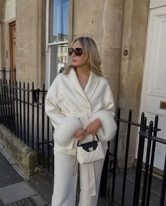 Detail of white wool coat featuring faux fur cuffs and a waist tie with a quilted bag
