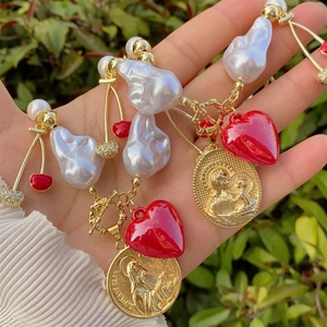 Baroque pearl necklace with 18k gold cherry and red heart charms in natural light