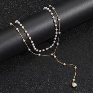 Detail of double-layer Y-shaped gold necklace with white pearls on a black pedestal