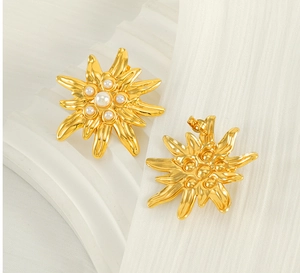 Detailed close-up of gold sunflower earrings with artificial pearls on a white texture