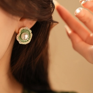 Détail de boucles d'oreilles feuille d'or avec émail vert et perle blanche sur modèle