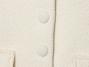 Dettaglio del blazer in tweed crema che mostra il tessuto e i bottoni ricoperti