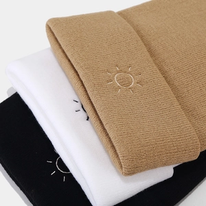 Detail of sun embroidery on stacked khaki, white and black knit beanies for winter