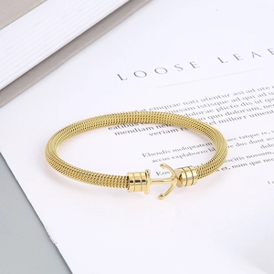 Detailed view of golden anchor clasp on a nautical mesh cable bracelet over a book