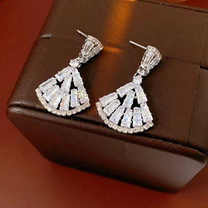 Close-up of silver fan-shaped earrings with clear sparkling zircon on a brown leather box