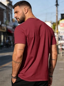 Back view of a man wearing a wine red crewneck cotton t-shirt in an outdoor street setting