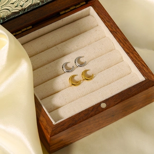 Detail of gold and silver crescent earrings in a luxury beige velvet wooden jewelry box