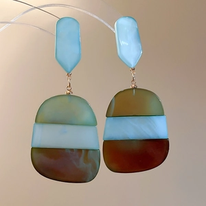 Detail of oval acetate drop earrings with blue resin top and marbled geometric pendants