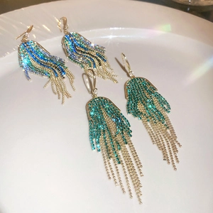 Detail of gold fringe earrings with vibrant blue and green crystals on a white ceramic plate