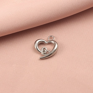 Macro shot of silver hollow heart pendant with crystal setting on pink fabric texture