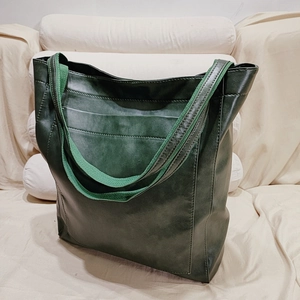 Vue détaillée du grand cabas en cuir vert foncé avec bandoulière sur tissu beige doux