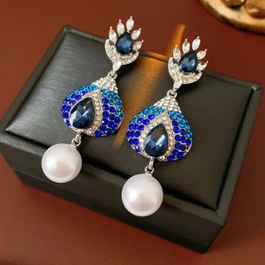 Dettaglio di orecchini vintage con strass blu e perle bianche su una scatola nera