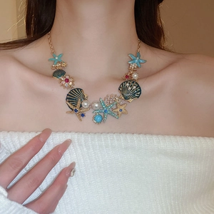 Detail of gold necklace featuring enamel starfish, green shells, and pearls on a model