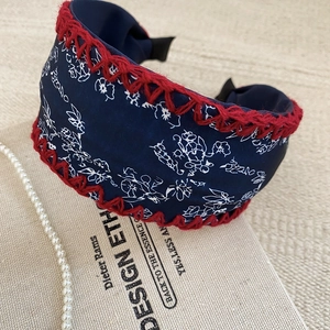 Close-up of wide floral knot headband with red hand-crocheted edges and pearls