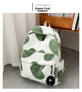 Detail of green and white cow print plush backpack with a fuzzy soot sprite pendant charm