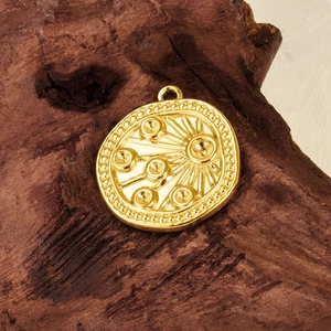 Detail of a golden stainless steel sun relief pendant on a dark rustic wooden surface
