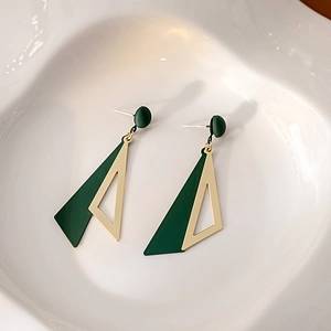 Macro detail of geometric green and gold triangle earrings on a white ceramic plate