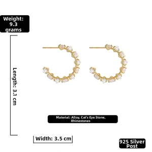 Detail view of gold C-shaped earrings with cat-eye stones, rhinestones, and 925 silver needles