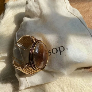 Macro shot of twisted gold wire woven cuff bracelet featuring a brown oval gemstone