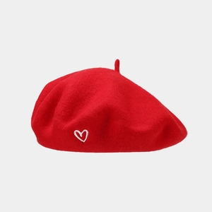 Detail shot of a red wool beret featuring a small white heart embroidery on the side