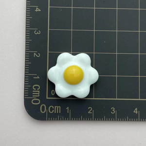 Detail showing white and yellow resin flower charm next to a centimeter measurement scale