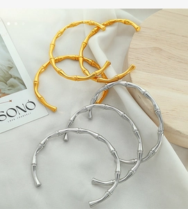 Detail of bamboo shaped stackable bangles in gold and silver finish on wooden base