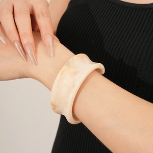 Detailed macro view of cream resin bangle with brown marble texture on model wrist