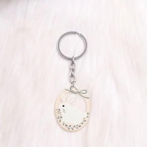 Close-up of cute acrylic white bunny keychain with a floral wreath on plush background