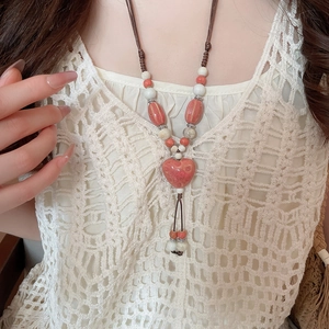 Détail d'un collier pendentif cœur en céramique rouge avec perles tissées sur fond de dentelle