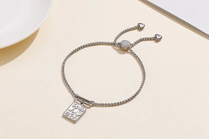 Detail of adjustable silver slider bracelet with rectangular charm and heart pendants