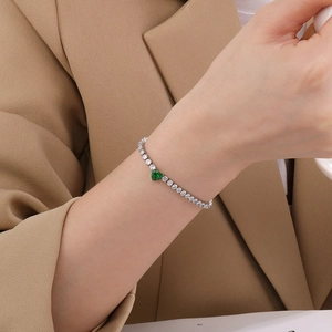 Detail of silver tennis bracelet with green heart-shaped stone on a female wrist