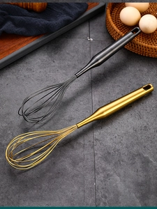 Detail of ergonomic handles on gold and black stainless steel hand whisks in kitchen set