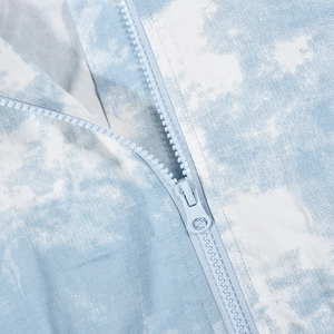 Dettaglio della cerniera azzurra e della trama del tessuto tie-dye sul capo di abbigliamento