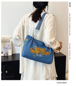 Detail of blue canvas tote bag with yellow 3D embroidery and metal chain strap