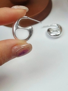 Macro detail of silver geometric pig nose earrings held by hand for scale