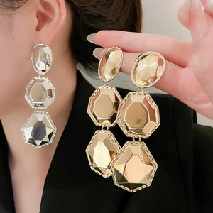 Gros plan de longues boucles d'oreilles métalliques facettées en finitions or et argent