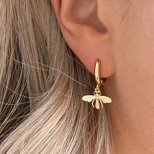 Close-up of golden bee pendant hoop earring on model with detailed wing texture