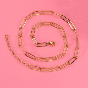 Detailed view of golden paperclip chain necklace with lobster clasp on pink background