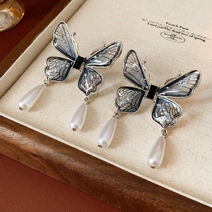 Detail of blue glitter butterfly earrings with delicate white pearl drop pendants