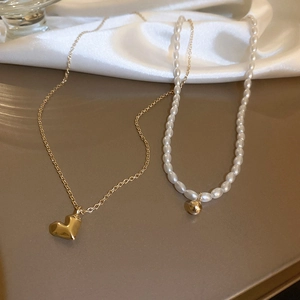 Détail d'un collier doré à cœur et ras du cou en perles sur tissu de soie doux