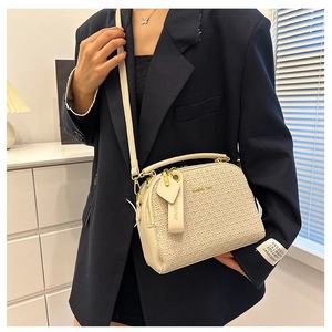 Detail of beige textured Boston bag with gold hardware worn with a navy blazer