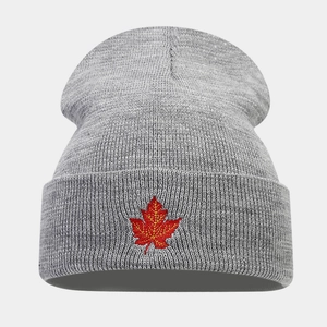 Close-up of red maple leaf embroidery on light grey knitted beanie showing fine texture
