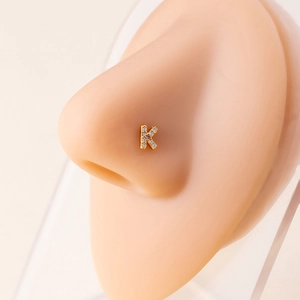 Close-up of a gold-plated initial K nose stud featuring cubic zirconia on a model