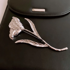 Macro detail of a silver tulip flower brooch pinned on a black leather handbag surface