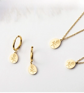 Detail of gold jewelry set with engraved rose pendants and earrings on white feathers
