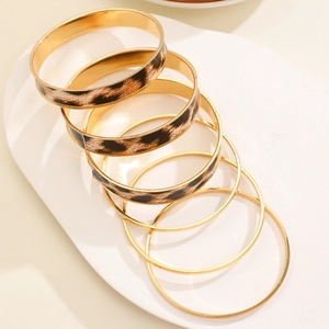 Detail showing stacked leopard print leather and gold-tone bangles on a tray
