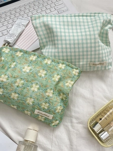 Portable plaid and floral green cosmetic bags for travel on a white bed background