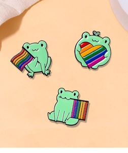 Detailed macro view of three enamel frog pins with rainbow pride flags on pink background