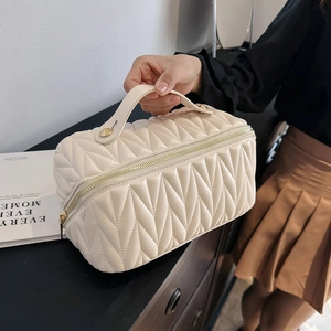 Grande borsa cosmetica trapuntata in pelle crema su un tavolo da trucco nero