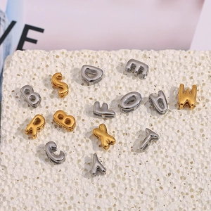 Perles alphabet creuses en acier inoxydable doré et argenté sur surface en pierre
